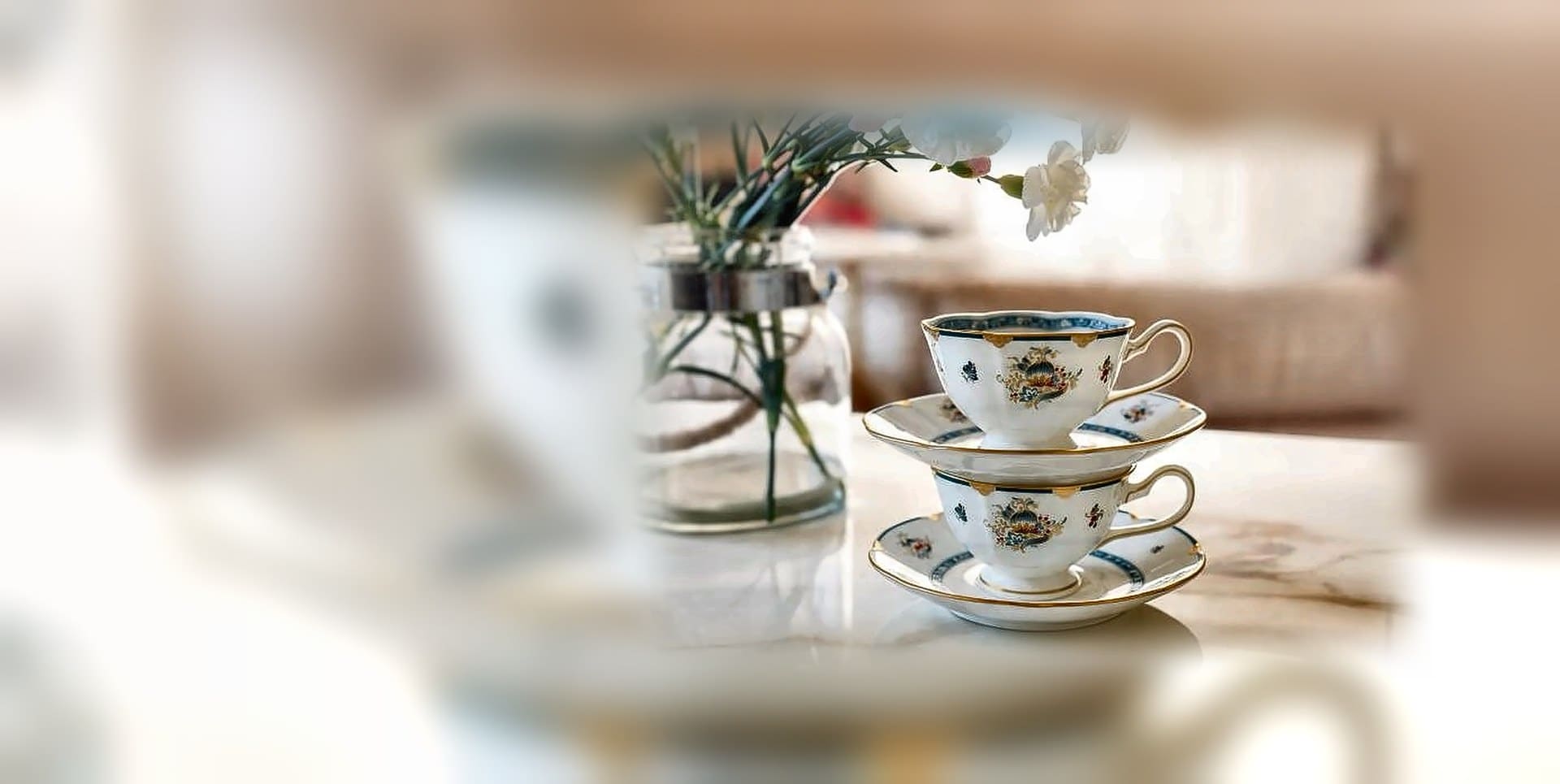 Two gold-rimmed bone china cups and saucers stacked beside fresh flowers