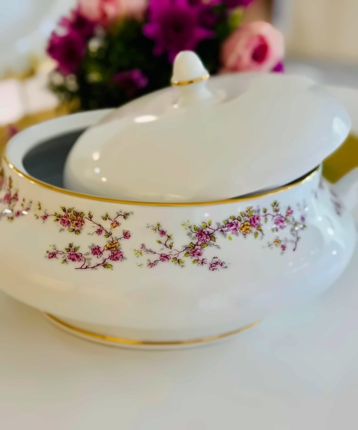 White serving tureen with a pink rose garland and gold rim, fresh flowers behind